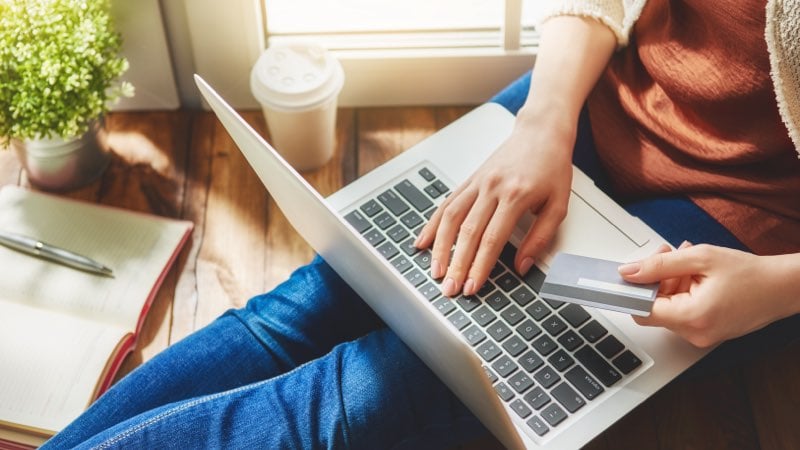 Pessoa com notebook e cartão na mão.