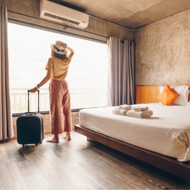 Imagem de uma mulher segurando uma mala de viagem em um quarto de hotel
