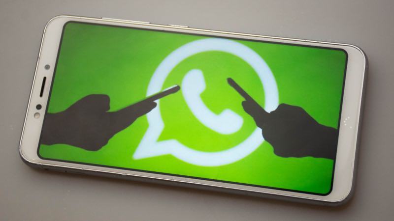 Tela de smartphone com símbolo do WhatsApp e silhuetas de duas mãos acessando um celular