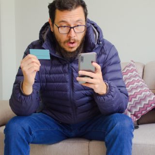 Imagem de um rapaz realizando compras online com seu cartão e smartphone nas mãos