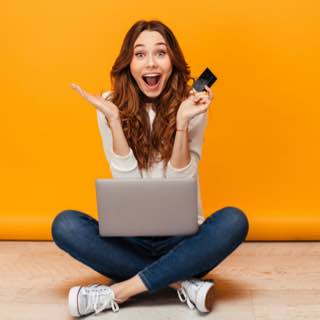 Mulher surpresa, sentada com notebook no colo e cartão na mão.