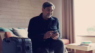 Zeca Camargo olhando para o celular ao lado da mala de viagem