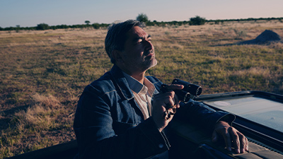 Zeca Camargo ao ar livre olhando pelo binóculo