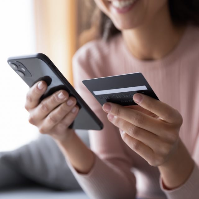 Imagem exibe mulher sorridente segurando cartão e smartphone. 