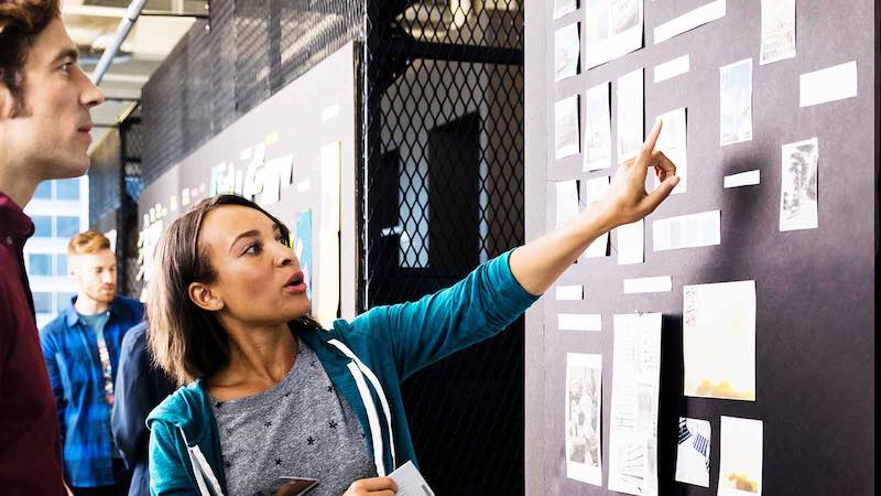 A pair of young designers discuss concepts posted on a presentation board.