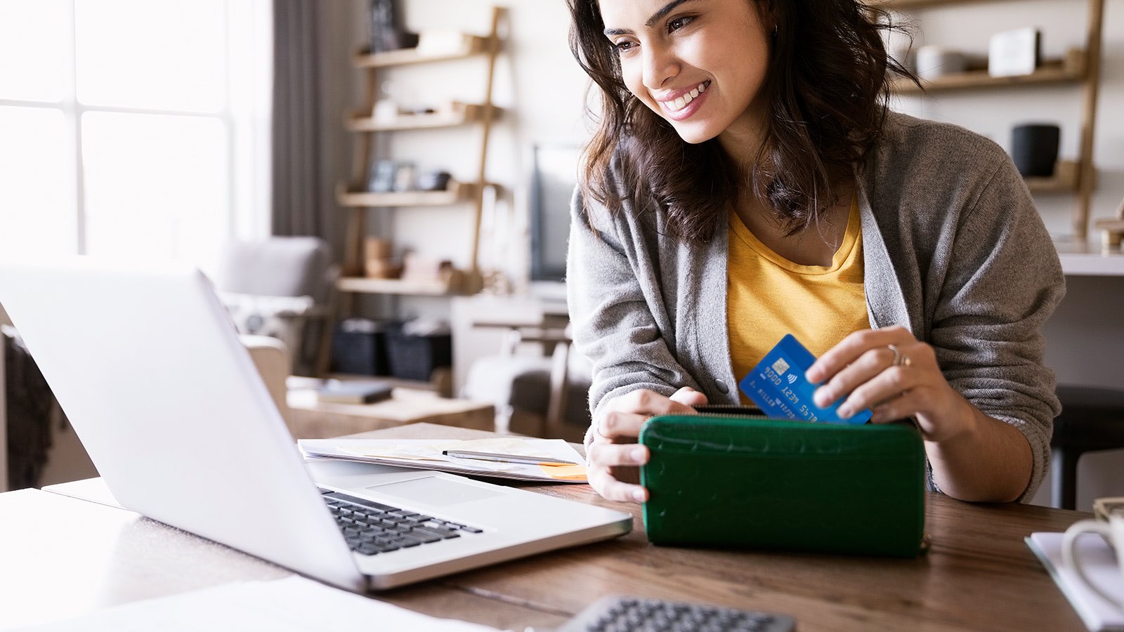 Smiling woman looking at laptop while pulling a contactless Visa card out of her wallet.