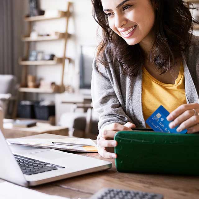 Smiling woman looking at laptop while pulling a contactless Visa card out of her wallet.