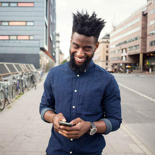 Smiling young man on the street looking at his phone.